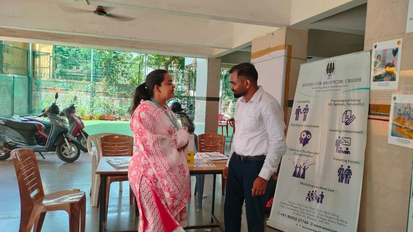 An IEC team member speaking with a visitor beside the IEC services banner at the Dream Marol event